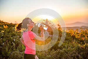 Thirsty woman trail runner drinking water from water bottle.