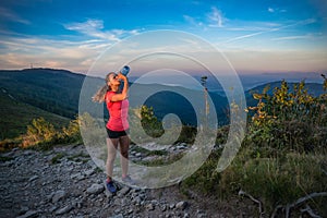 Thirsty woman trail runner drinking water from water bottle.