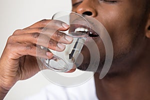 Thirsty young african man holding glass drinking water, closeup view