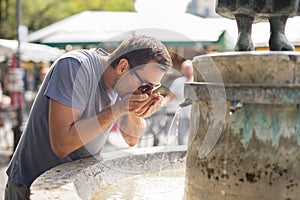 Thirsty young casual cucasian man drinking water from public city fountain on a hot summer day