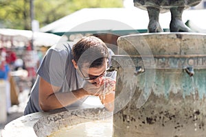 Thirsty young casual cucasian man drinking water from public city fountain on a hot summer day