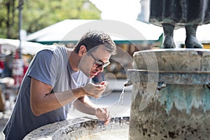 Thirsty young casual cucasian man drinking water from public city fountain on a hot summer day