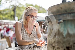 Thirsty young casual cucasian woman drinking water from public city fountain on a hot summer day