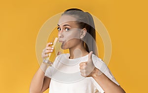 Thirsty young woman drinking fresh orange juice and gesturing thumb up