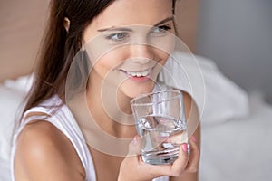 Thirsty young woman holding glass drinking water in bed