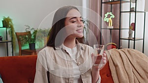 Thirsty young woman sitting at home holding glass of natural aqua make sips drinking still water