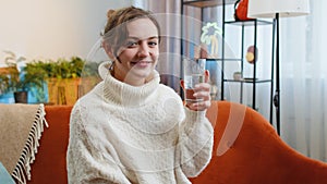 Thirsty young woman sitting at home holding glass of natural aqua make sips drinking still water