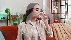 Thirsty young woman sitting at home holding glass of natural aqua make sips drinking still water