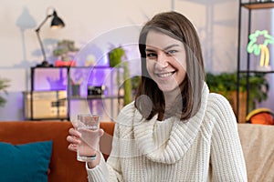 Thirsty young woman sitting at home holding glass of natural aqua make sips drinking still water