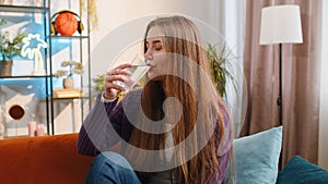 Thirsty young woman sitting at home holding glass of natural aqua make sips drinking still water