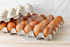 Thirty brown chicken eggs in a cardboard tray packaging on a white wooden table. Raw fresh hen eggs in a carton box. Ingredient