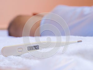 Thirty-nine degrees on medical thermometer and infant asleep on White mattress.