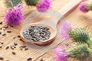 Thistle seeds in wooden spoon and flowers on rustic background