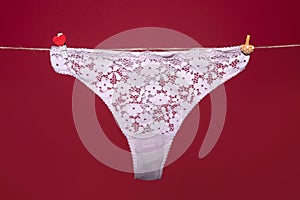 Thong bikini panties, white lace underwear lingerie on rope isolated on red background.