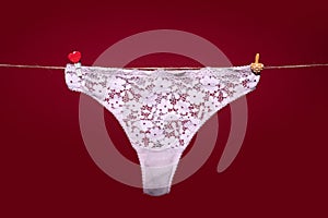 Thong lace bikini panties, white sexy underwear lingerie on rope isolated on red background.