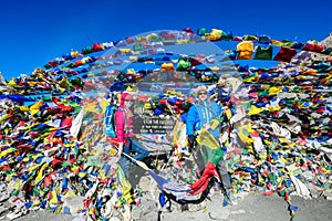 Thorung La Pass - A couple standing between prayer flags on top of the pass