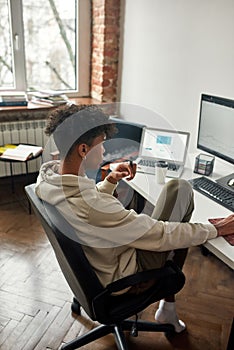 Thoughtful african american broker analyzing stock graph on pc screens and vaping