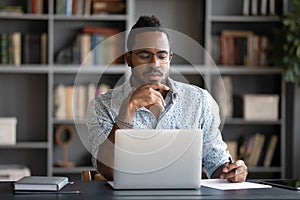 Thoughtful African American businessman looking at laptop screen, touching chin