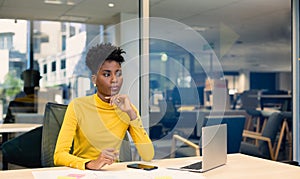 Thoughtful african american businesswoman sitting with mobile phone and laptop at desk in workplace