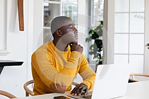 Thoughtful african american man using laptop at home and looking away