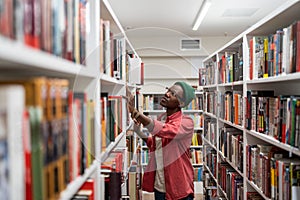 Thoughtful African American student man in glasses choosing book in college library or bookstore