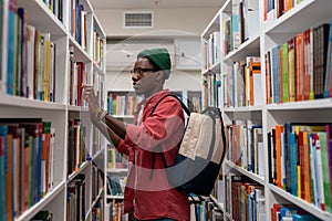 Thoughtful African American student man in glasses choosing book in college library or bookstore