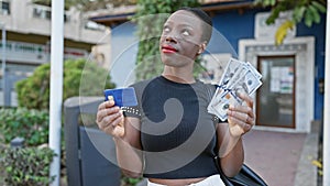 Thoughtful african american woman pondering over dollars and credit card on city street