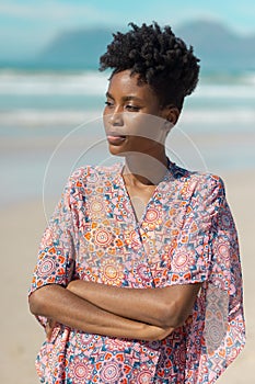 Thoughtful african american young woman with short curly hair and arms crossed standing at beach