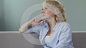 Thoughtful aged female having rest on couch at home, enjoying good memories