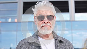 Thoughtful aged man looking at camera while standing outside