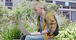 Thoughtful albino african american man with dreadlocks sitting in park using laptop