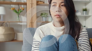 Thoughtful Asia lady sit embracing knees at sofa in living room at house look outside with feel lonely, Sad depressed teenager