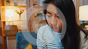 Thoughtful Asia lady suffering from insomnia sit at sofa in living room at house night with feel lonely, Sad depressed teenager