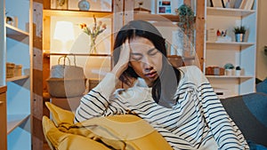 Thoughtful Asia lady suffering from insomnia sit at sofa in living room at house night with feel lonely, Sad depressed teenager