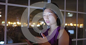 Thoughtful asian businesswoman using tablet and looking out of office window at night, slow motion