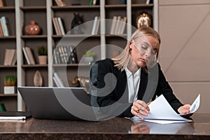 Thoughtful attractive businesswoman wearing formal wear sitting reading contract
