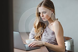 Thoughtful attractive girl drinking coffee and using laptop