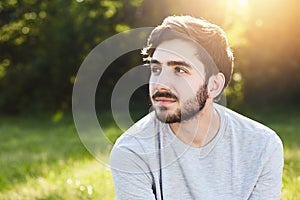 Thoughtful attractive male with dark mustache and beard looking aside into distance dreaming about something pleasant while relaxi