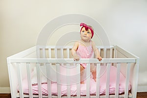 Thoughtful baby girl stand in the crib bed smiling