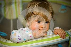 Thoughtful baby in playpen biting her fingers