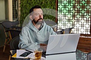 Thoughtful bearded man in casual clothes in cafe using laptop. Online business
