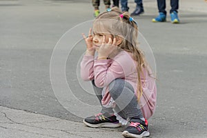 A thoughtful and beautiful blonde girl of 4-5 years old is squatting in the middle of an asphalt street