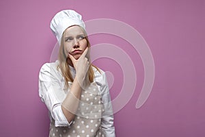 Thoughtful beautiful girl cook in kitchen clothes thinks over an idea on a pink background, a woman housewife dreams and looks at