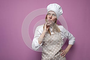 Thoughtful beautiful girl cook in kitchen clothes thinks over an idea on a pink background, a woman housewife dreams and looks at