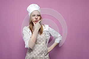 Thoughtful beautiful girl cook in kitchen clothes thinks over an idea on a pink background, a woman housewife dreams and looks at