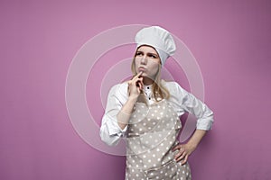 Thoughtful beautiful girl cook in kitchen clothes thinks over an idea on a pink background, a woman housewife dreams and looks at