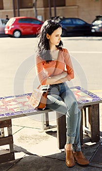 Thoughtful beautiful girl sitting down on a street bench