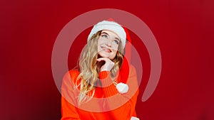 a thoughtful beautiful woman in a Santa Claus hat on a red background.