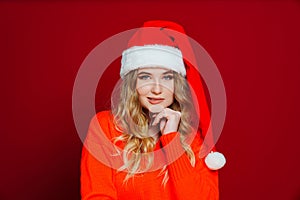 a thoughtful beautiful woman in a Santa Claus hat on a red background.