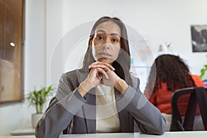 Thoughtful biracial businesswoman sitting at desk making video call in modern office